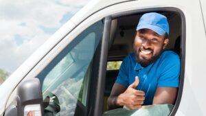 smiling african american delivery man showing thumb up from van