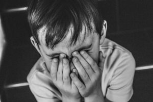 Little boy hiding his face with his hands.