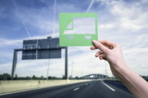 Hand holds green logistics symbol against highway