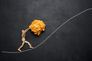 A wooden figurine of a person rolling a crumpled paper ball upwards, concept of perseverance